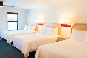 Habitación de hotel con 3 camas con sábanas blancas en Two Sunsets Hotel, en Panguitch