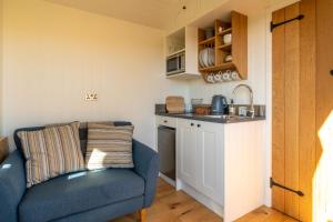 a living room with a blue couch and a kitchen at Scalderskew Shepherds Hut in Gosforth