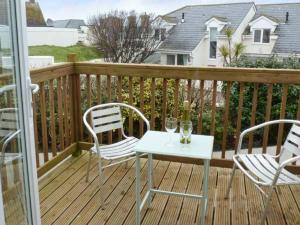 een houten terras met 2 stoelen en een tafel met wijnglazen bij Beachcombers in Newquay