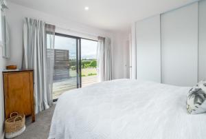 a white bedroom with a bed and a large window at Relax on the Deck in Martinborough  +18 photos