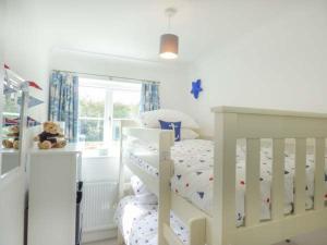 a white bedroom with a white crib with a teddy bear at 7 Harlyn Cottages in St Merryn