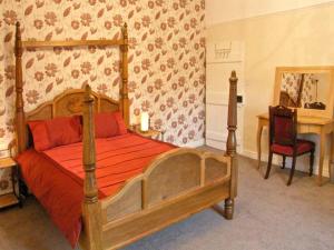 1 dormitorio con cama de madera con sábanas rojas y escritorio en Hendre Aled Farmhouse en Llansannan