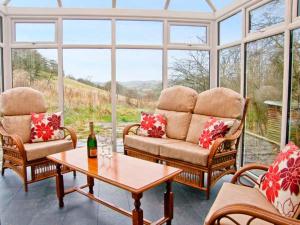 un salón acristalado con 2 sillas y una mesa con una botella de vino en Hendre Aled Farmhouse en Llansannan
