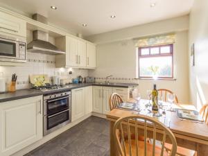 uma cozinha com armários brancos e uma mesa de madeira em Ridge Cottage em Longwitton