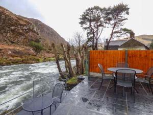 a patio with tables and chairs next to a river at 4 Adwy'r Nant in Beddgelert