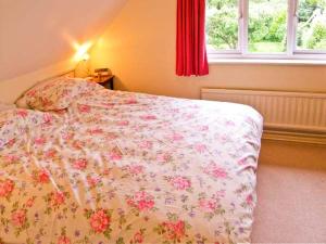 a bedroom with a bed with a floral bedspread and a window at Brock Cottage in Beaulieu