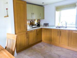 una cocina con armarios de madera y fregadero en Muirmailing Cottage en Plean