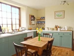 eine Küche mit einem Holztisch mit Stühlen und einer Vase aus Blumen in der Unterkunft Coles Cottage in Holsworthy