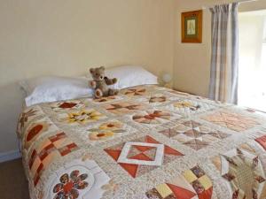 a teddy bear sitting on a bed with a quilt at Coles Cottage in Holsworthy
