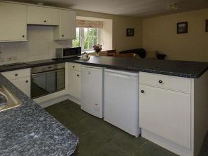 uma cozinha com armários brancos e um balcão preto em Cockley Beck Cottage em Coniston