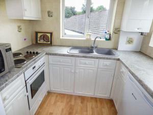 a kitchen with white cabinets and a sink and a window at Moorside in Horrabridge
