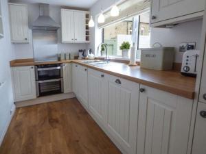 a kitchen with white cabinets and a wooden floor at Silversands Cottage in Amble