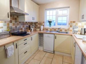 a kitchen with white cabinets and a sink and a window at Ty Woods Cottage in Rhoscolyn