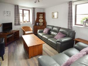 a living room with a leather couch and a tv at Fairwater Mill Cottage in Kingsteignton