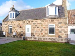 a stone house with a grass yard in front of it at Coastal Cottage in Inverallochy