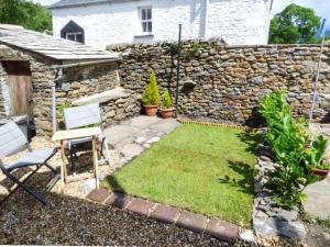 a garden with a stone wall and a chair at Fells Cottage in Sedbergh
