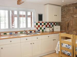 uma cozinha com armários brancos e um lavatório em Little Beeches em Selattyn