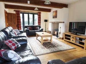 a living room with a leather couch and a television at Carthorse Cottage in Luton