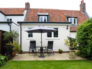 un patio avec une table, des chaises et un parasol dans l'établissement Mrs Dale's Cottage, à Clenchwarton