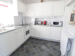a white kitchen with white cabinets and appliances at Trigfa Cottage in Abersoch