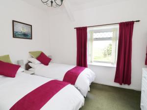two beds in a room with red curtains and a window at Trigfa Cottage in Abersoch