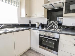 Una cocina con gabinetes blancos y un horno de estufa. en Coastal Cottage, en Reighton