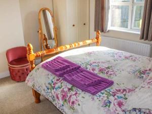 a bed with a purple blanket on it with a mirror at Primrose Cottage in Alford