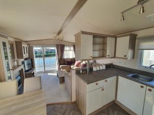 a kitchen with white cabinets and a living room at Cosy caravans Meadow lake Golden Palm Resort in Chapel Saint Leonards