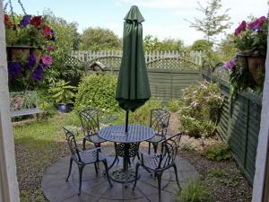 einen Tisch und Stühle mit einem grünen Sonnenschirm auf einer Terrasse in der Unterkunft Railway Cottage in Fairbourne