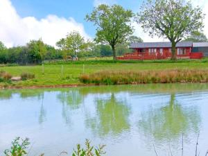 a house in a field next to a body of water at Lake View Lodge in Shepton Mallet