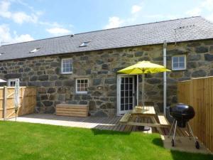 a patio with an umbrella and a grill in front of a stone house at Y Stabal in Chwilog