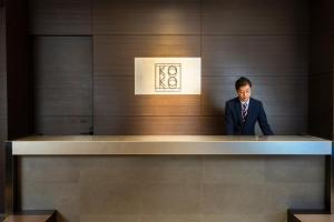 福岡市にあるKOKO HOTEL 福岡天神のスーツ姿の男がカウンターに立っている