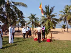 un grupo de personas parados alrededor de un poste de bandera en la playa en Goldi Sands Hotel, en Negombo