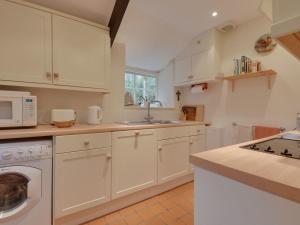 eine Küche mit weißen Schränken, einer Spüle und einem Geschirrspüler in der Unterkunft Lew Quarry Cottage in Lewdown
