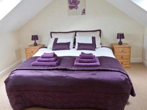 a bedroom with a large bed with purple sheets and pillows at Summer Farm Cottage in Bedale
