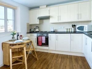 Isle of WhithornにあるThe Clamshellの白いキャビネットと木製テーブル付きのキッチン