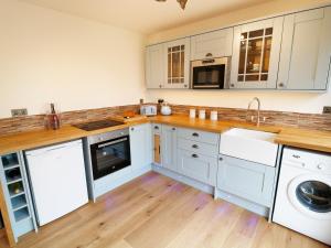 cocina con armarios blancos, lavadora y secadora en Northlands Country Cottage With Hot Tub, en Plymouth