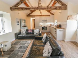a living room with a leather couch and a kitchen at Rhianwen, Plas Moelfre Hall Barns in Llangadwaladr