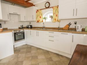 サドベリーにあるStable Cottageの白いキャビネットと壁掛け時計付きのキッチン