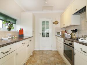 una cocina con armarios blancos y fregadero en Sheila's Cottage, en Penryn