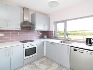 cocina con armarios blancos, fregadero y ventana en Labasheeda en Kilrush