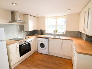 cocina con armarios blancos, lavadora y secadora en Manor Farm House Cottage, en Kettering