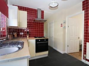 a kitchen with a sink and a red tiled wall at Smallcroft in Whitstable