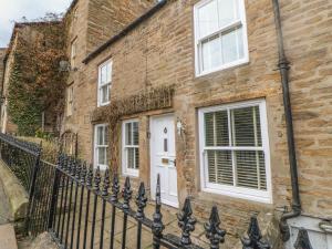 ein Backsteingebäude mit einer weißen Tür und einem Zaun in der Unterkunft Bank Cottage in Alston