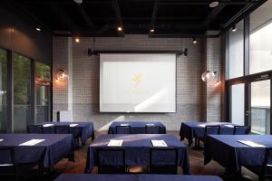une salle de conférence avec des tables bleues et un écran de projection dans l'établissement L7 Myeongdong, à Séoul