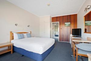 a bedroom with a bed and a desk and a tv at Banjo Paterson Motor Inn in Lakes Entrance