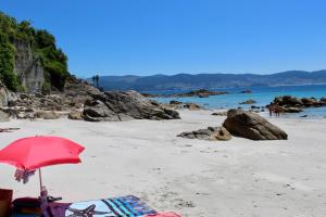 a beach with a red umbrella and chairs on the sand at Hostal Casa Aurita Adults Only in Sanxenxo
