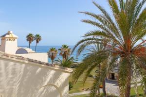 a palm tree next to a white wall and the ocean at Beach apartment La Cala in La Cala de Mijas