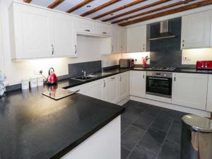 uma cozinha com armários brancos e um balcão preto em Cornel Clyd em Llanddulas