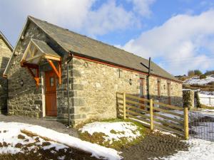 a stone building with a wooden door in the snow at Ty Isaf Penrhyddion in Betws-y-coed